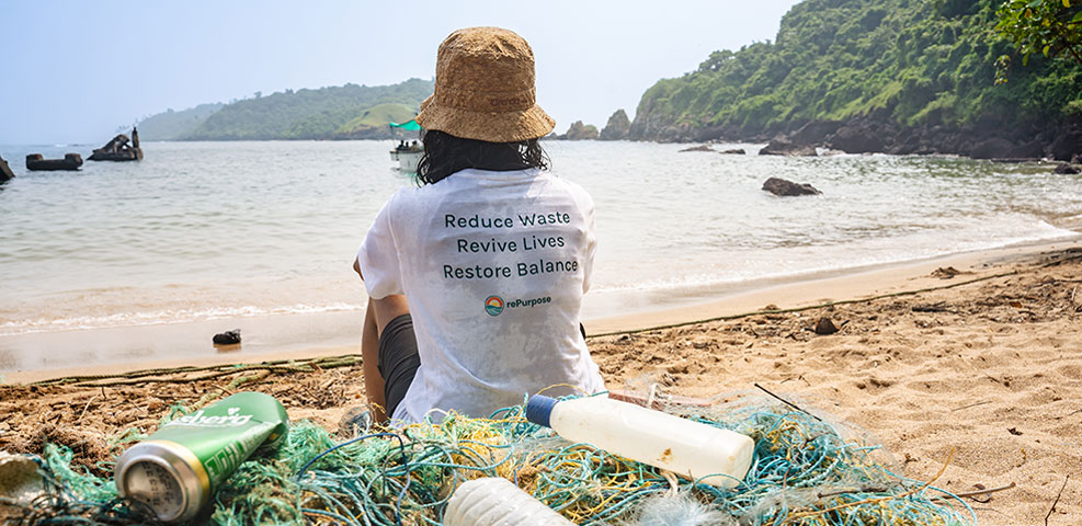 Woman sitting on beach working with rePurpose Global to recover plastic from the environment.